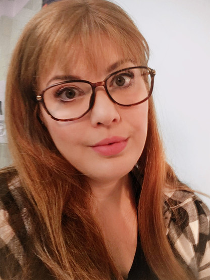 Red-haired nerd Tatyana Larina looks straight into the camera. She has long hair with bangs, wears glasses and a black and white plaid flannel shirt. (Megan Marie Hart in costume, wig and makeup for the first act of Eugene Onegin at Staatstheater Darmstadt. Costume: Julia Burkhardt; Photo: Megan Marie Hart, CC BY-SA 4.0)
