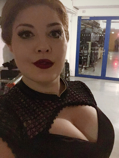 Red-haired Princess Tatyana Gremina looks directly into the camera. She has her hair up and wears a high-necked black top with a keyhole neckline that shows her décolleté. (Megan Marie Hart in costume, wig and makeup for the third act of Eugene Onegin at Staatstheater Darmstadt. Costume: Julia Burkhardt; Photo: Megan Marie Hart, CC BY-SA 4.0)