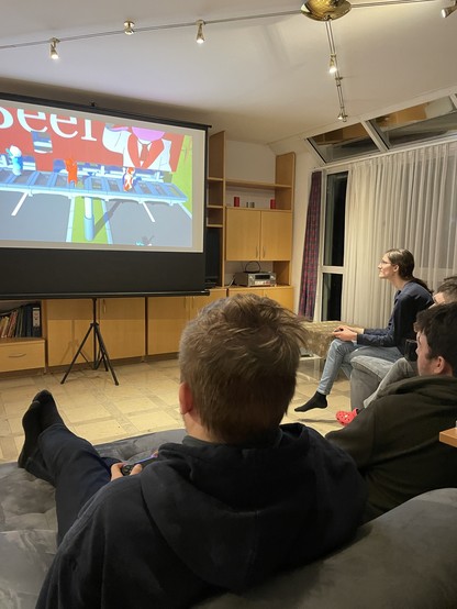 Vier Leute sitzen auf dem Sofa und spielen mit Controllern gegeneinander.