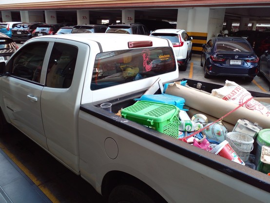 a pickup truck, the back filled with all kinds of boxes and garbage and stuff, on the back window is a manga-style cartoon sticker of an ample young lady wearing a cowboy hat 