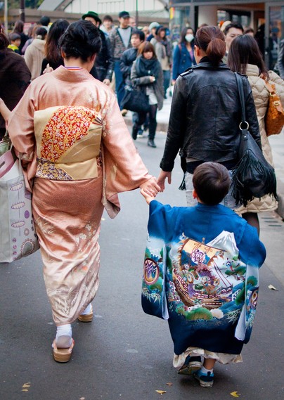 A boy dresses in a traditional overcoat for New Year, the material emblazoned with auspicious images (such as Mt Fuji and the Treasure Boat).