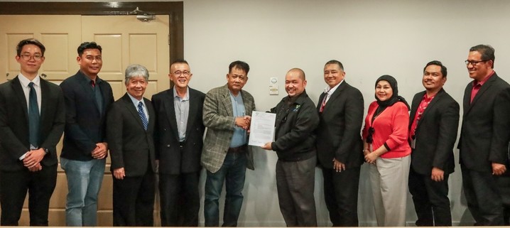 Two people holding Letter of Award with the others witnessing. / Photo from linked article.