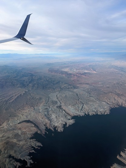 View from an airplane window of the edge of a lake with desert and sky in the background. 