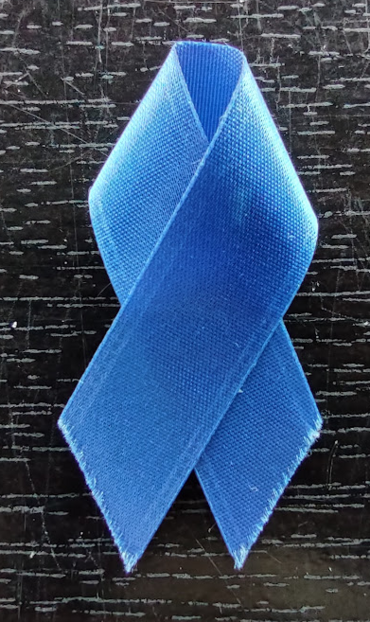 Photo: A blue ribbon with frayed edges on a scratched piece of black lacquered wood. Sunlight illuminates the grain in the wood. 