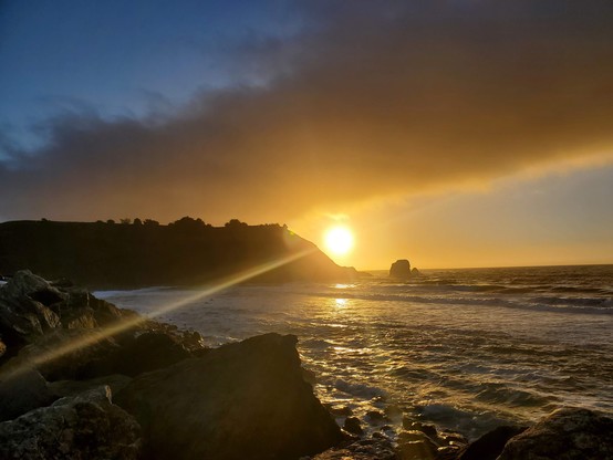 Old Sol playing peek-a-boo, with a lovely promontory over to the side.  The ocean is visible below.