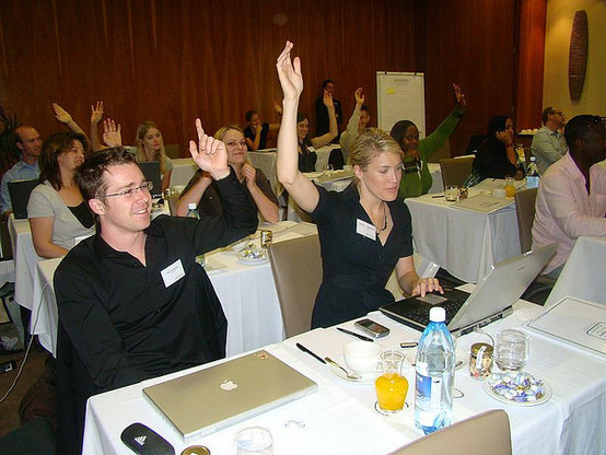 right way to vote: photograph of conference attendees sitting in front of tables, raising their hands to vote