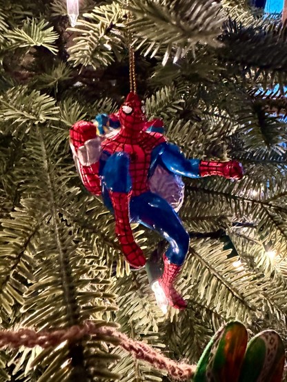 A Spider-Man ornament hangs from a Christmas tree. 