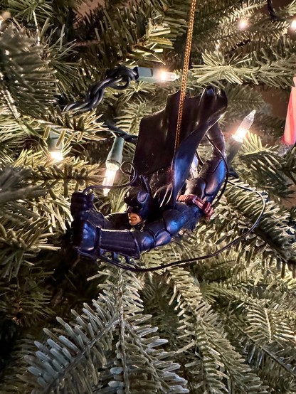 A Batman ornament hangs from a Christmas tree. 