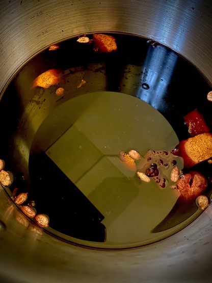 Looking into the pot of Glögi simmering on the stovetop. Purple liquid with ingredients floating on the top.
