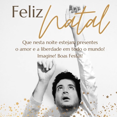 Homem branco de cabelos pretos olha pra cima e estende os braços para o alto. na legenda, em tons dourados: "Feliz natal. Que nesta noite estejam presentes o amor e a liberdade em todo o mundo! Imagine! Boas festas!". No fundo da foto, estrelas douradas.
