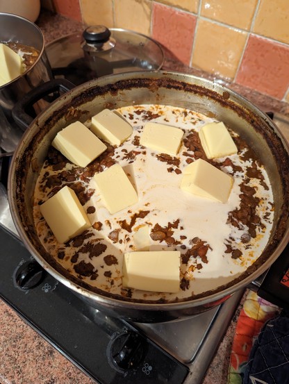 A large steel pan, there's a brown lentil stew dish but it's mostly covered up by several blocks of butter and a lot of cream waiting to be stirred in. 