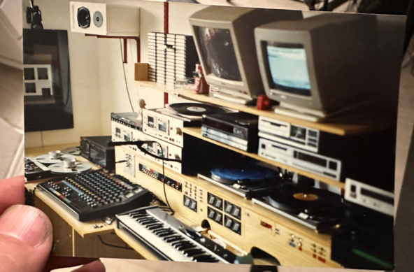 Setup 1993:
Bildbeschreibung von Bing:

Das **Foto von 1993** zeigt eine **Sammlung von Audio- und Computerausrüstung**. Hier sind einige Details:

1. **Monitore**: Zwei **CRT-Monitore** sind sichtbar. Einer zeigt Text oder Code, während der andere ausgeschaltet ist.
2. Mischpult: Ein Mischpult mit verschiedenen Knöpfen und Schiebereglern zur Audio-Steuerung ist zu sehen.
3. Keyboard-Synthesizer: Ein Keyboard-Synthesizer mit schwarzen und weißen Tasten steht im Vordergrund.
4. Audioausrüstung: Mehrere Audiogeräte, darunter Kassettendecks und e Plattenspieler mit einer Vinylplatte darauf, sind auf Regalen gestapelt.
5. Lautsprecher: Lautsprecher sind an der Wand über dem Ausrüstungssetup montiert.
6. Raum: Der Raum hat weiße Wände, und ein Fenster mit teilweise sichtbaren Jalousien ist im Hintergrund.

