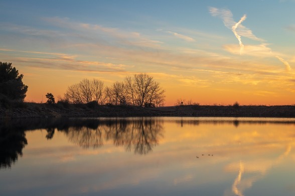 Se puede ver un atardecer en un pequeño lago donde hay algunos árboles que se reflejan en el agua.

You can see a sunset in a little lake where there are some trees which are reflected in the water.