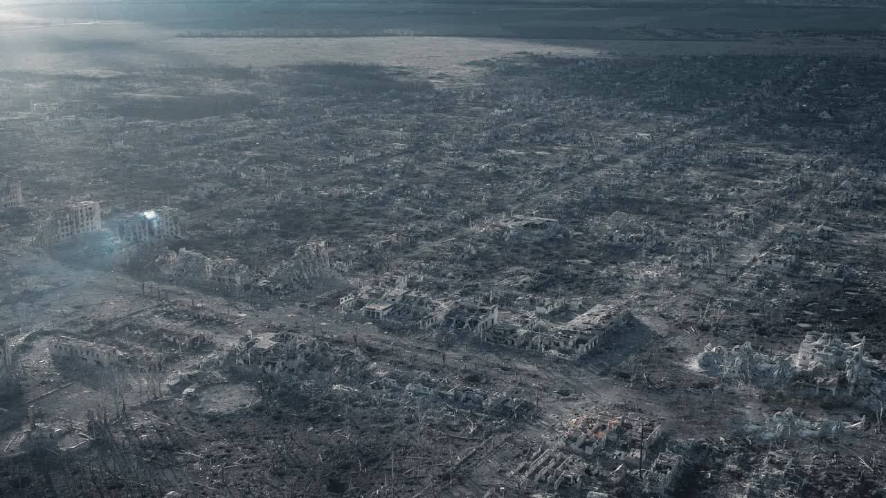 The image shows a vast expanse of destruction. It appears to be an aerial view of a city that has been completely devastated. The landscape is bleak and gray, with the ruins of buildings scattered as far as the eye can see. There are no signs of life or intact structures, just endless rubble and decay. The sky is overcast, adding to the somber and desolate atmosphere of the scene.