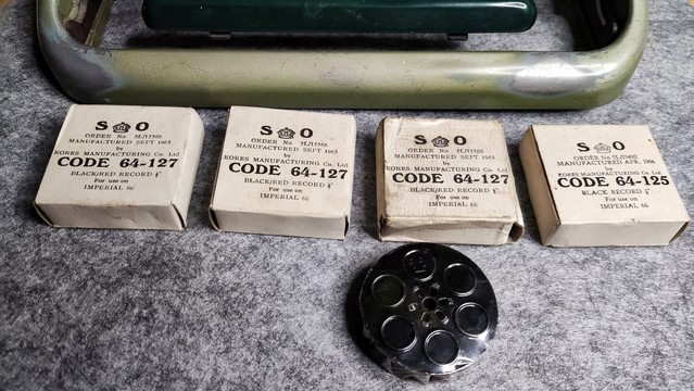 A typewriter spool below 4 boxes of the same size below the front of a typewriter.

