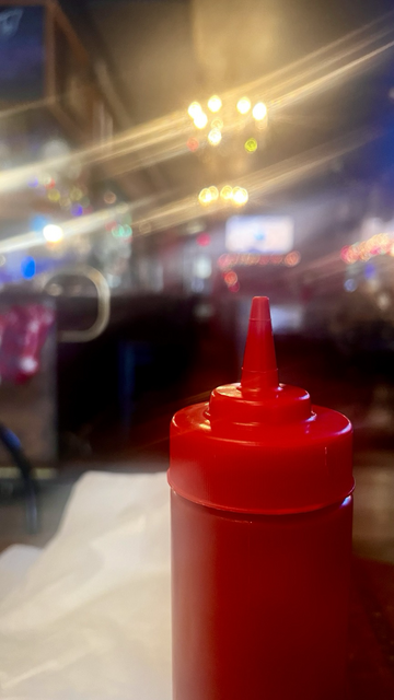 Red ketchup squeeze bottle, soft focused dive bar atmosphere behind. Square 5 Public House, Blacksburg, VA.  