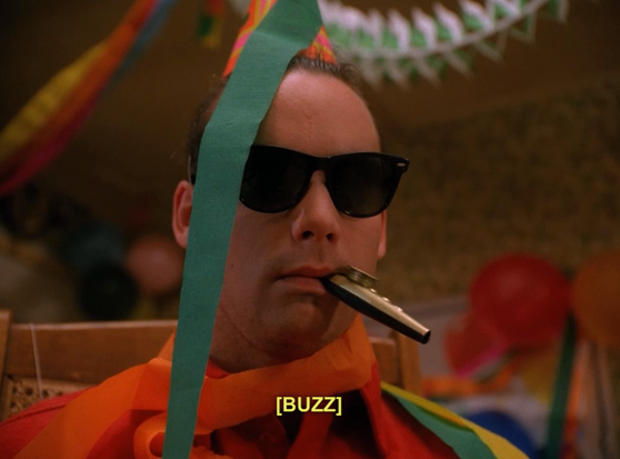 Comatose Leo Johnson wearing sunglasses and a conical party hat buzzing a kazoo.