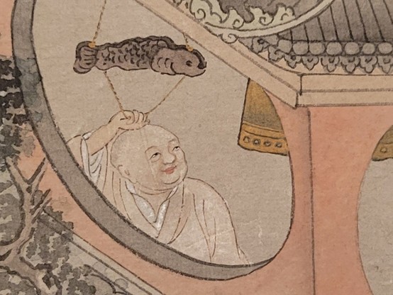 Close-up of a mural showing a smiling person in robes inside an enclosure with a large bell suspended from the ceiling. The person holds a swinging beam in the shape of a fish, and seems in the motion of striking the bell.