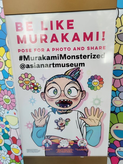 Freestanding sign encouraging visitors to advertise the exhibit on social media. It reads in red block letters, "Be Like Murakami! Pose for a photo and share". Next in black it reads, "#MurakamiMonsterized @asianartmuseum"

The sign has a white background with a handful of rainbow-colored daisies and stars. The main focus is an AI-generated cartoon representation of Takashi Murakami, shown smiling with both hands raised at the elbow and waving. The person wears a white shirt with blue sleeves, with a mouse-like cartoon character holding a cartoon daisy flower, with a lightning-bolt tail. The person has a mouth full of pointed, rainbow-colored teeth, rainbow-colored hair pulled back into a ponytail, blue-green eyes, and large round glasses. 

Text at bottom describes the process in the steps connected by arrows: 1, at left) "The Original Photo" (photo of Takashi Murakami in similar pose). 

2 at center) "The illustration was generated using the Lora model of Murakami's self-portrait in an AI called stable diffusion" (pencil sketch showing various facial expressions with arrows pointing to composite body sketch)

3 at right) "The AI-generated  illustration" (final cartoon shown above)