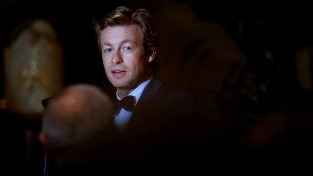 Patrick Jane (Simon Baker) in a tuxedo looking over his shoulder in a dimly lit room in a scene from The Mentalist TV show.
