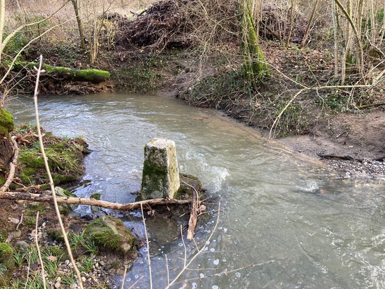 The border stone is actually surrounded by water on all four sides, as the river has carved around it. The border passes through the middle of the stream.