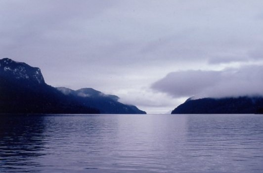 Low rain filled clouds obscure the hilltops across this lake, and the overcast sky turns everything dark or steel grey.