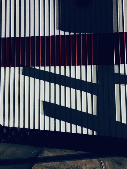 A street sign shadow on a metal wall. The wall has ridges and is white with a red stripe. 