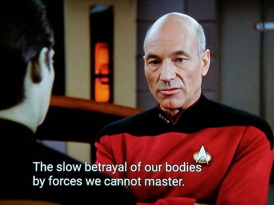 TNG scene. We're on the bridge and looking at Captain Picard just over Data's shoulder. Picard looks lost in thought. Closed caption reads, "The show betrayal of our bodies by force we cannot master."