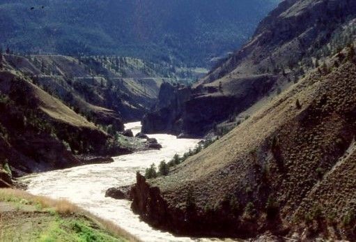 A turbulent and rapid filled river winds its way through it canyon. Steep sloping hills surround the river, and high hills beyond enclose the entire scene.  