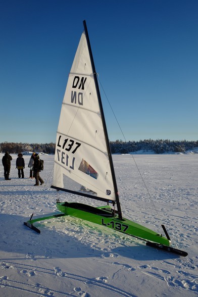 A green DN class iceboat on sea ice on a sunny day.