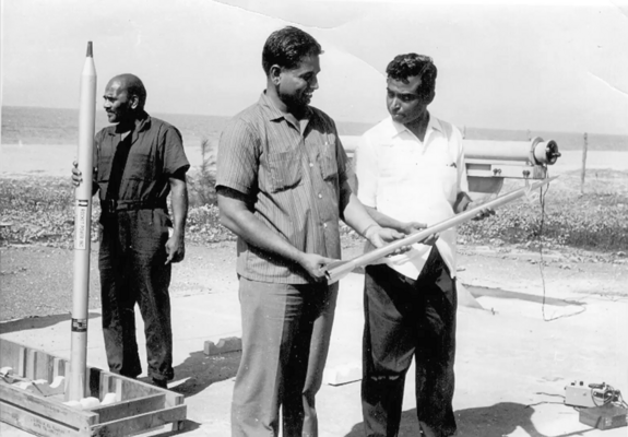 Image showing three people. Two inspecting a rocket and one in background unboxing it.