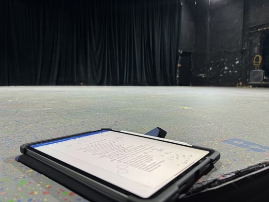 A tablet with documents against the backdrop of a theater stage with drawn curtains.