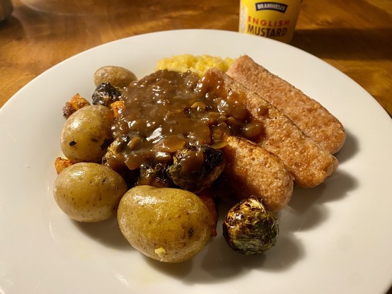 Plate of Sosmix sausages with brussels sprouts, carrots, potatoes, swede mash and homemade gravy. English mustard visible behind