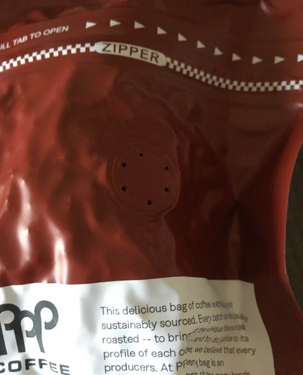 Six holes in a circle on the back of a bag of coffee indicate the one-way valve in the coffee bag. This is clearly the back of the 'vacuum packed' coffee seen in the other photo.