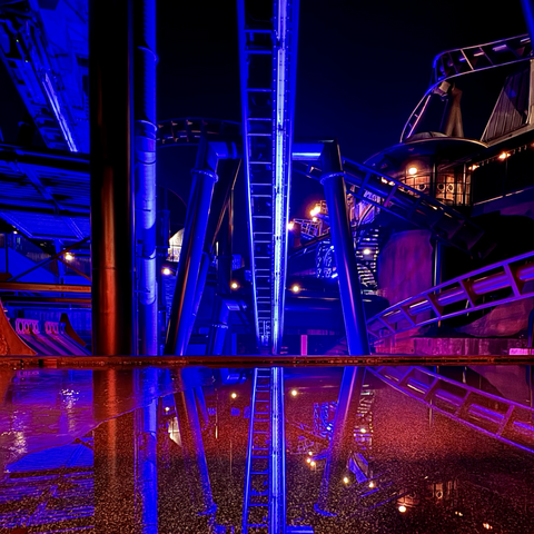 F.L.Y.’s second launch at night. The track reflects in a pool of water. Bright blue and red lights illuminate the track. 