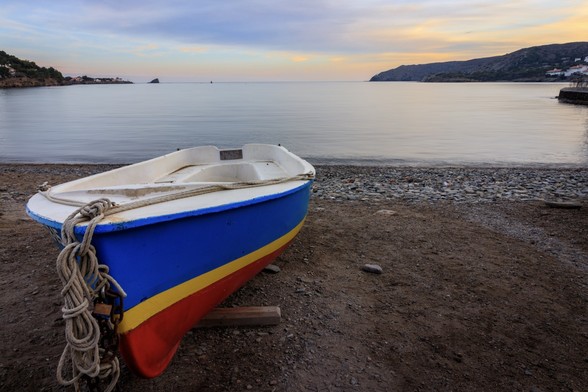 Se puede ver una barca en primer plano en la zona izquierda en la playa de Cadaqués (Girona). Al fondo se ve el mar en calma y el atardecer.

You can see a boat in a beach in the foreground at Cadaqués (Girona). At the background you can see a calm sea and sunset sky.