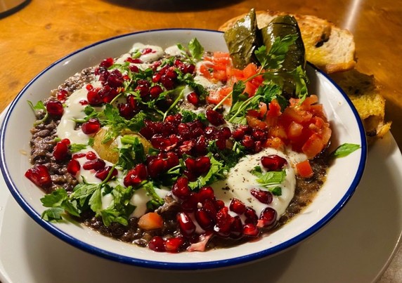 Rummaniyeh - a Palestinian lentil-aubergine-pomegranate dish - which is a brownish stew topped with fresh parsley, pomegranate and vegan yogurt, served with vine leaves, some chopped tomato and toasted olive bread