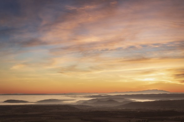 Se puede ver un atardecer con un cielo de nubes anaranjadas y algo rojizas y un paisaje bajo algunas nubes.

You can see a sunset with an orange sky and a low lands with some clouds.