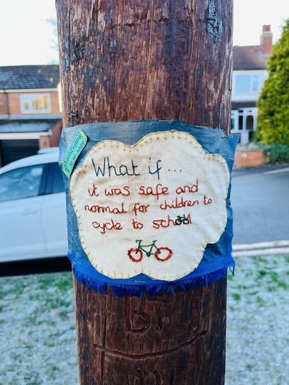 An embroidered cloth attached to a telegraphy pole. The stitching says: what if… it was safe and normal for children to cycle to school. #LeedsDreams for our future