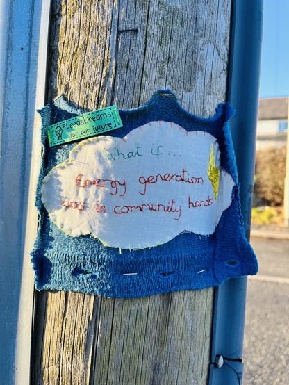 An embroidered cloth attached to a telegraphy pole. The stitching says: what if… energy generation was in community hands. #LeedsDreams for our future