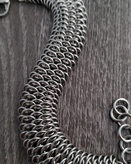 a stainless steel bracelet made with the dragonscale chainmaille weave laying flat on a charcoal gray wood desktop with a couple of bends in the chain