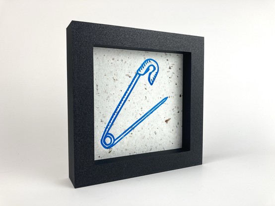 A framed relief print of a safety pin.