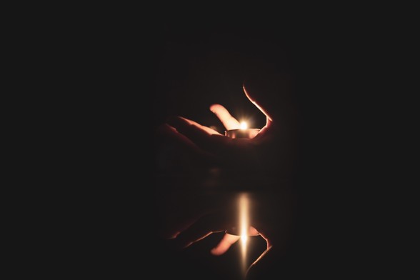 Se puede ver una mano en la oscuridad sosteniendo una vela encendida en su palma.

You can see a hand in the darkness holding in its palm a candle.