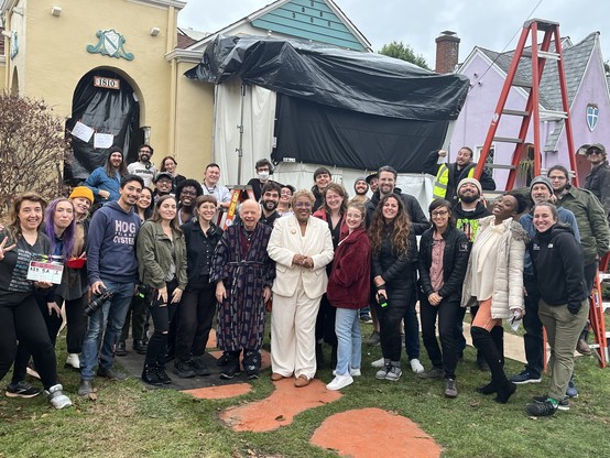 
A group of filmmakers stand in front of a house covered in filmmaking ephemera.