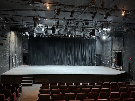 An empty theater with a stage, red seats, and stage lighting equipment.