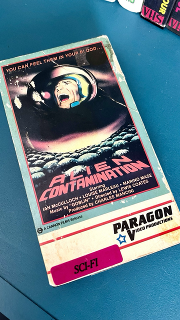 VHS tape of Alien Contamination sitting atop a blue end table. 