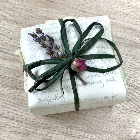 A small package, beautifully wrapped with lavender and rose buds. It’s shown on a light wooden background.