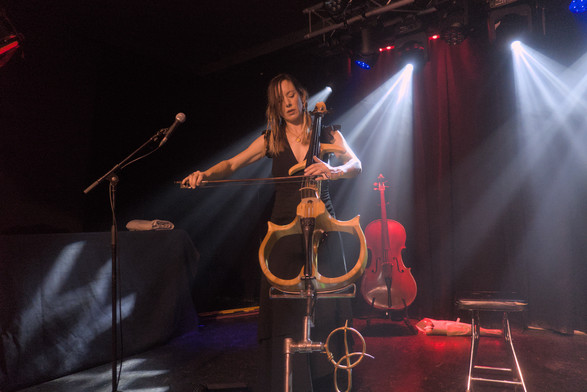 Jo Quail playing a skeletal structured electric cello on stage.