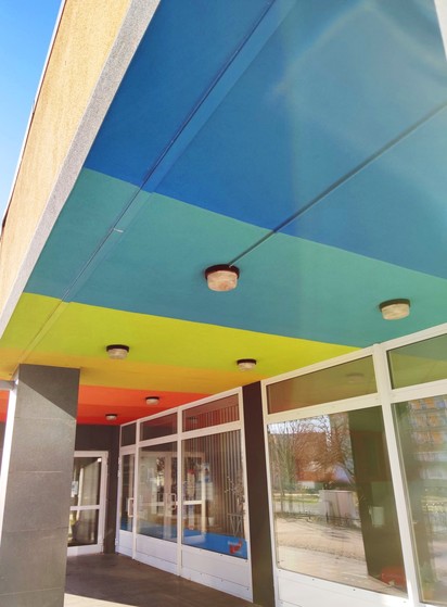 Büro der AfD in Hoyerswerda von außen. Eine weiße Fensterfront, beklebt mit dem Logo der AfD im unteren Bereich. Die Decke ist mit breiten farbigen Streifen bemalt. 

Ein Regenbogen! 