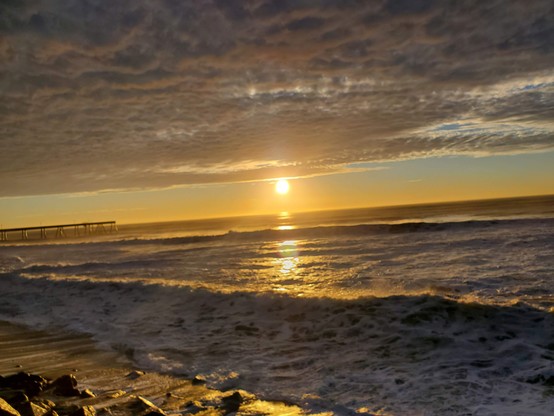 Old Sol doing its shiny-fiery thing.  What looks like a cloud quilt up above, and a few people on the beach below.